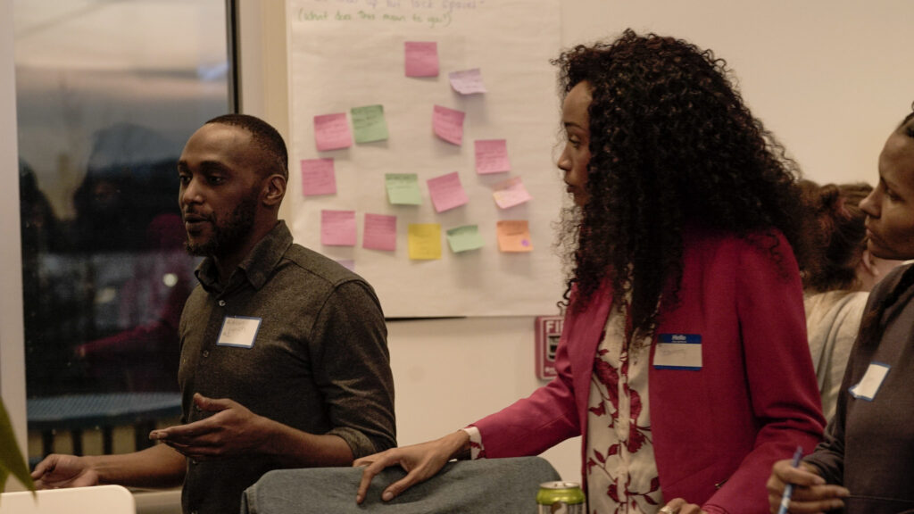 Adrian K. Lynch participating in a collaborative workshop discussion beside a board of colorful notes.